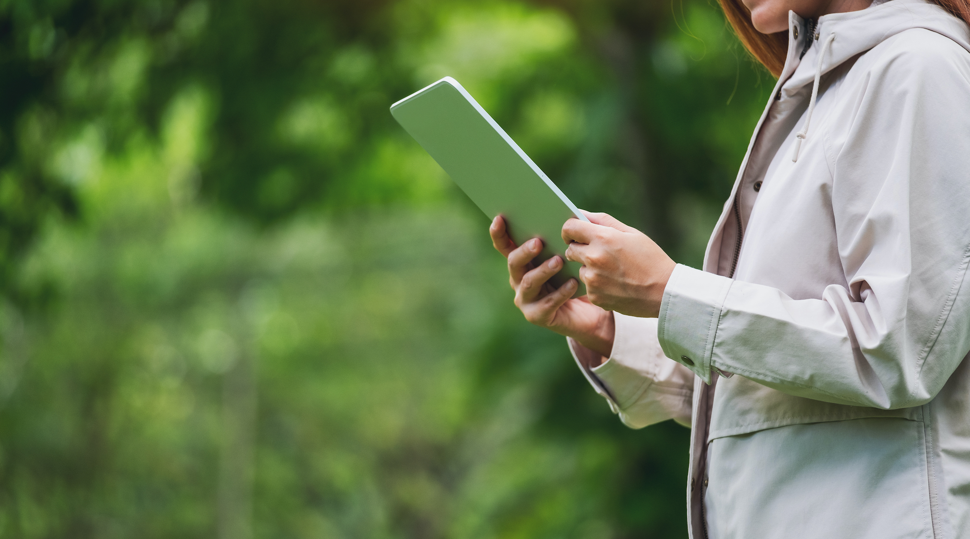 Closeup image of a young woman holding and using digital tablet in the outdoors